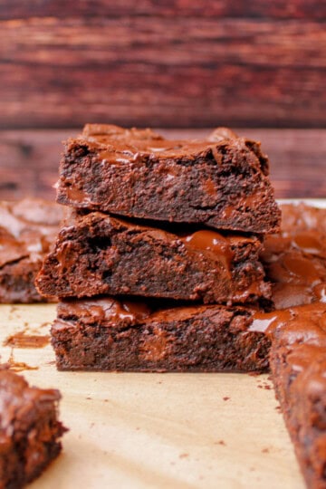 A batch of the best fudge brownies freshly baked in a metal pan with a shiny crinkle top and melted chocolate chips, sliced into squares.