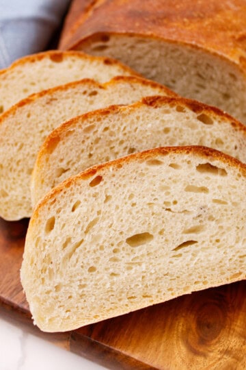 Freshly baked golden brown French bread loaves cooling on a wooden cutting board