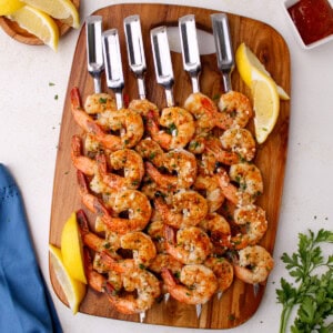 A top-down view of juicy garlic butter grilled shrimp skewers garnished with fresh parsley and served with fresh lemon slices and cocktail sauce.